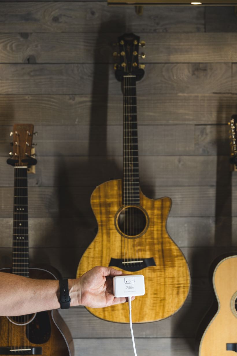 Hand holding PuzL Detect in a music room with guitars on the wall