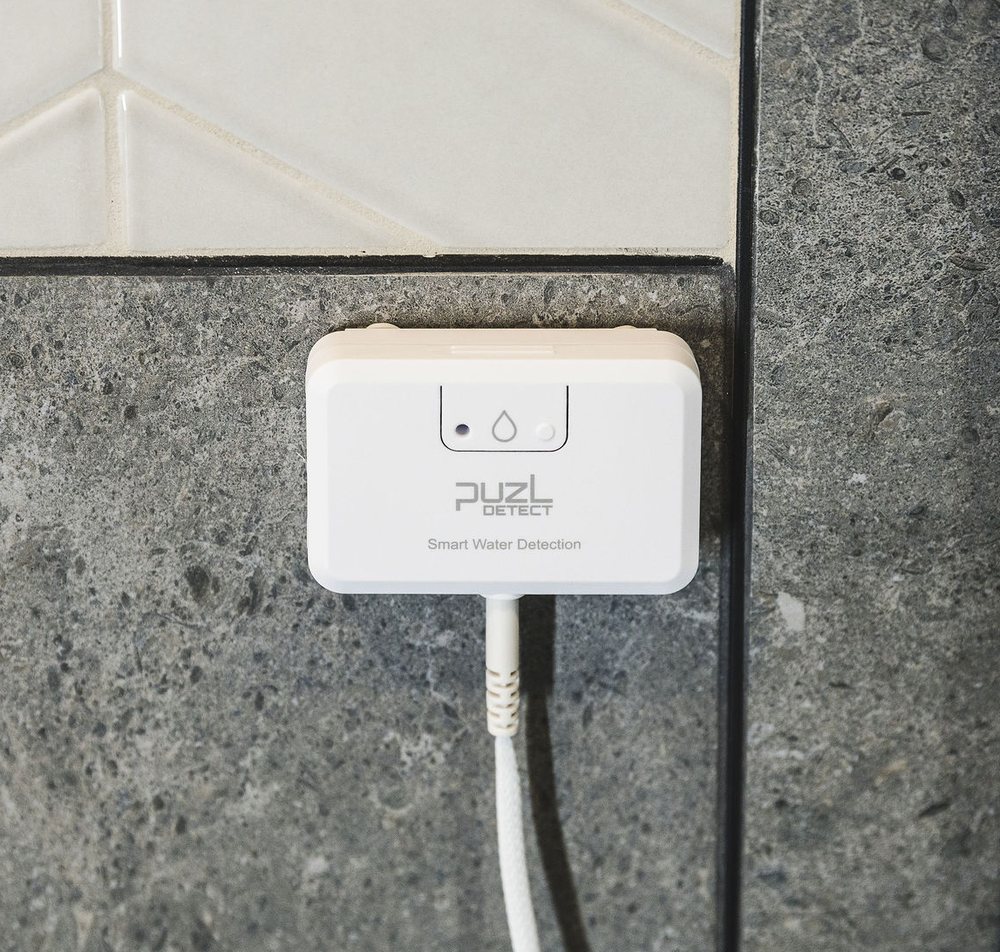 PuzL Detect unit mounted on a wall, front view, showing the alert LED and pairing button